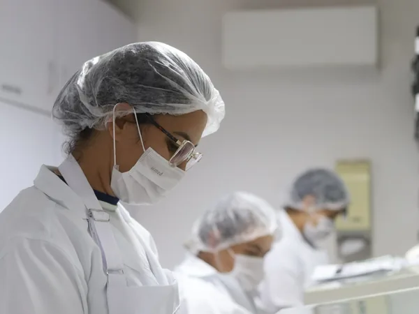 Equipe da Pharmativa paramentada preparando fórmulas na bancada do laboratório