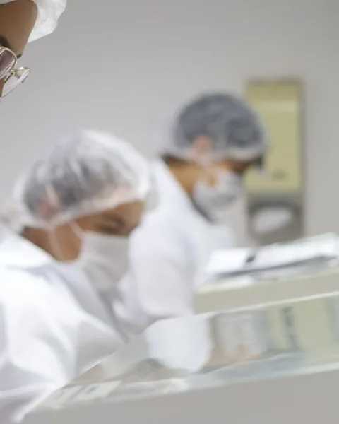 Profissionais com touca e máscara trabalhando na bancada do laboratório da Pharmativa